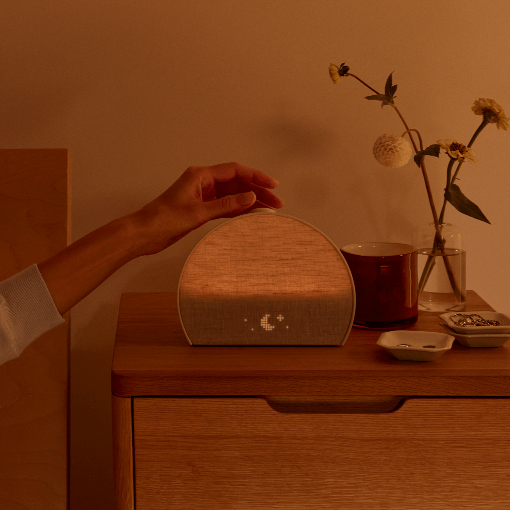Restore 3 on a bedside table with a hand turning the volume knob