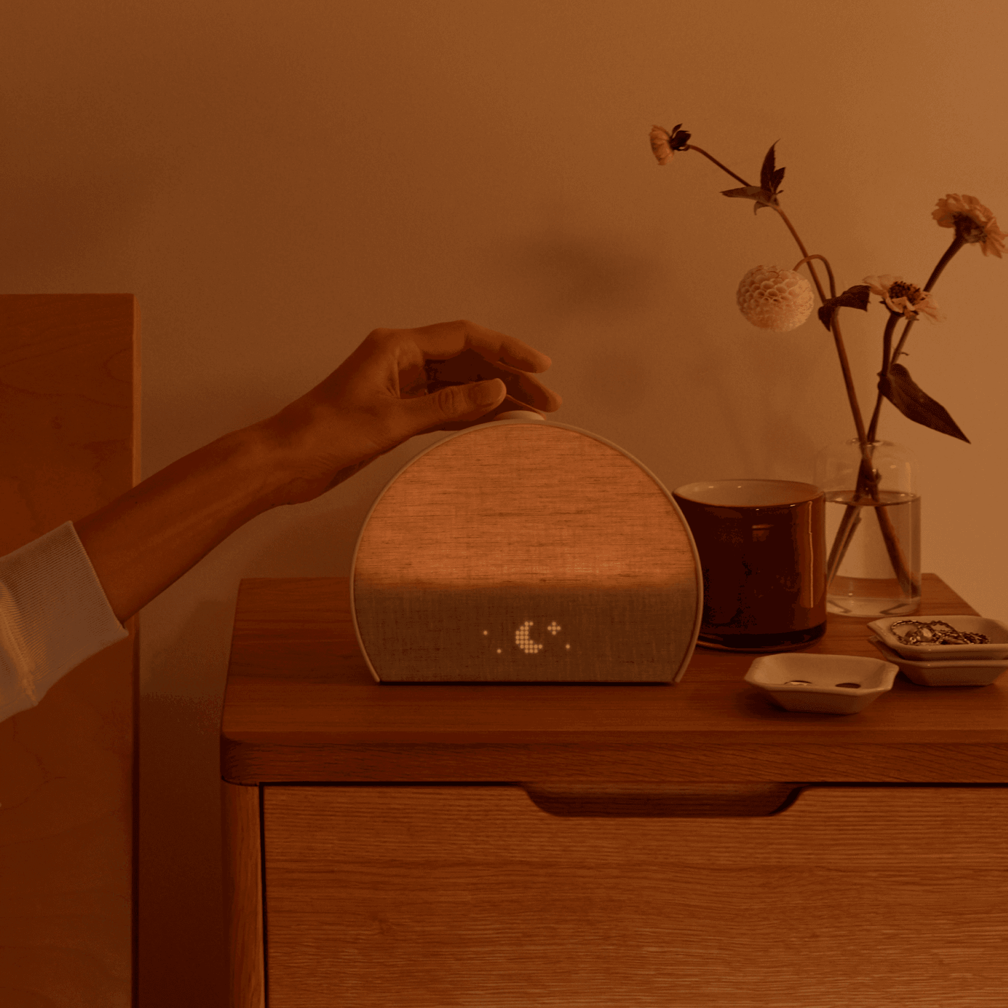 Restore 3 on a bedside table with a hand turning the volume knob