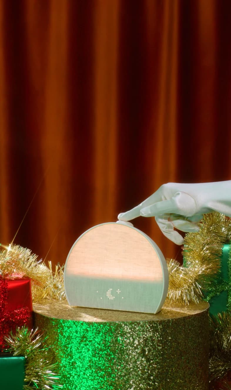 Hand tapping the top button on a Hatch Restore 3 with a holiday gift background