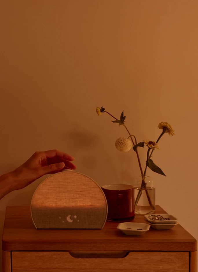 Hand tapping the top button of a Restore 3 on a nightstand